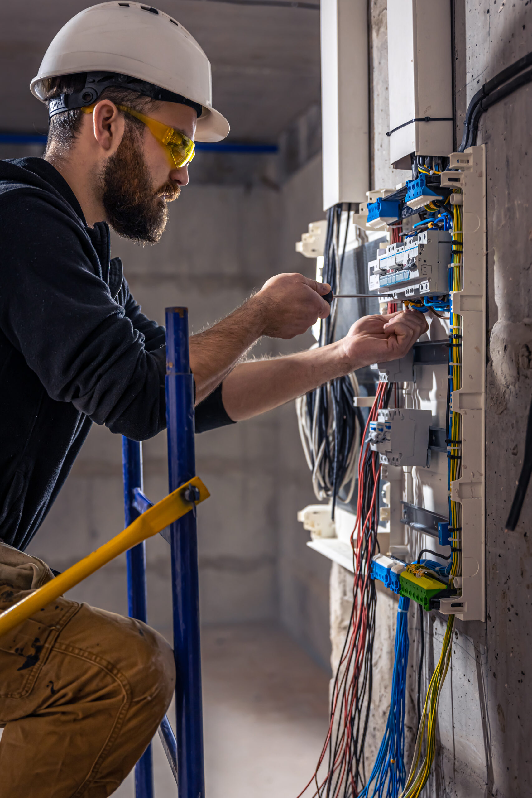 A male electrician works in a switchboard with an electrical connecting cable, connects the equipment with tools.
